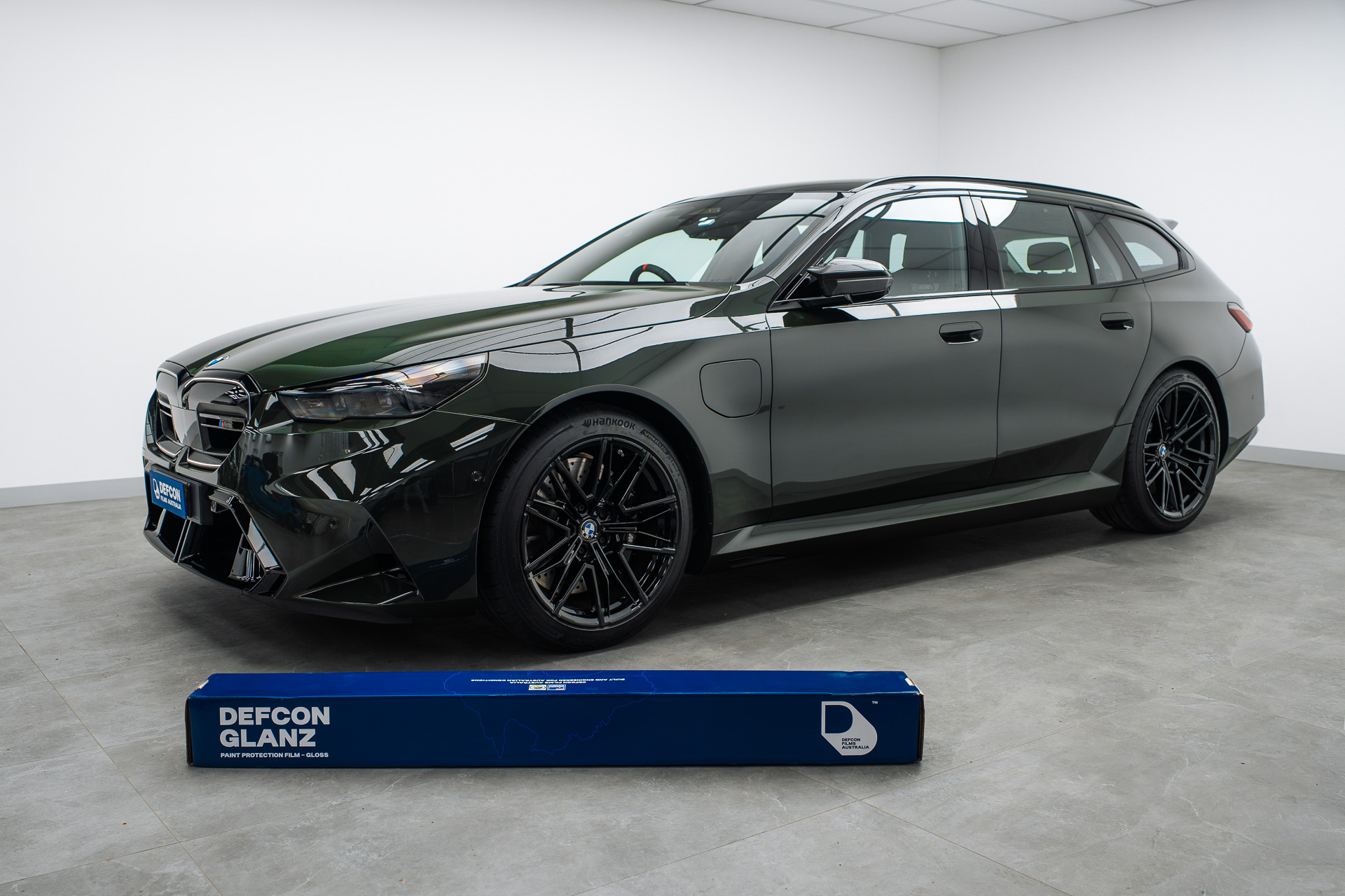 Side profile of a dark green BMW M5 Touring wagon with a Defcon Films Australia Defcon Glanz gloss paint protection film box